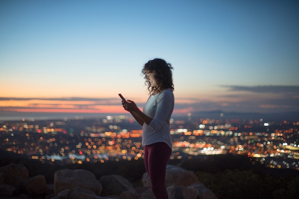 Materializing Solutions – Woman looking at phone above a city